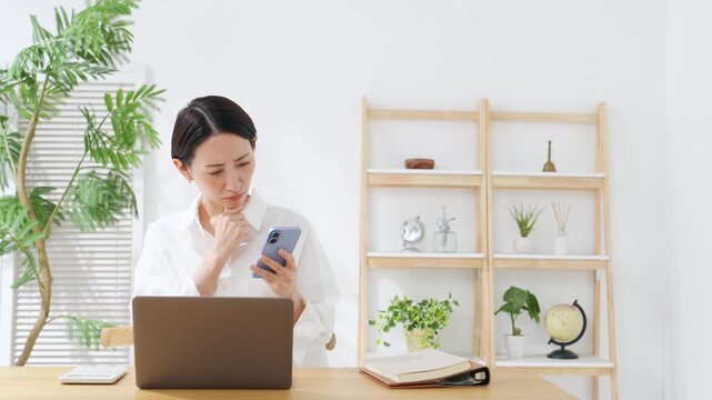 スマホとノートPCを見ながら悩むミドル女性。アプリ、疑問、考える、不安、心配、不満、SNS、家計