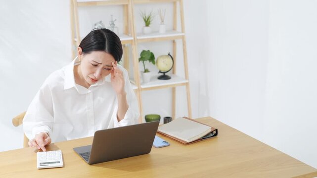 ノートパソコンを見ながら考えるミドル女性。悩み、不満、不安、心配、家計、困る、問題、疑問、電卓、簿記