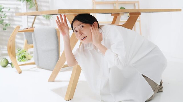 テーブルの下に潜る女性。地震、災害、非難、防災、驚く、怯える、怖い、緊急地震速報