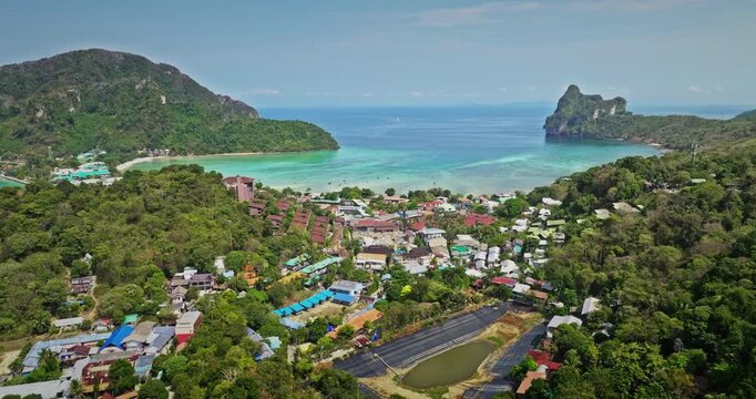 Phi Phi Don island village between towering limestone karsts and vibrant turquoise waters of Andaman Sea. Amazing tropical landscape, travel and explore Thailand's nature. Aerial view drone flight