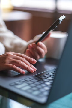 Vertical closeup image of a woman using smart phone and laptop computer in cafe