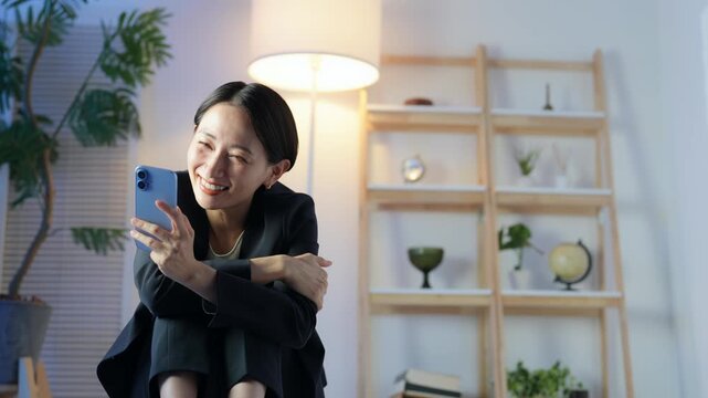 暗い部屋でスマホを見るミドル女性。夜更かし、夜中、動画、SNS、笑顔、チャット、恋愛、孤独、独身