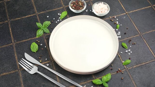 Empty plate with basil leaves, salt, and pepper on dark tiled background