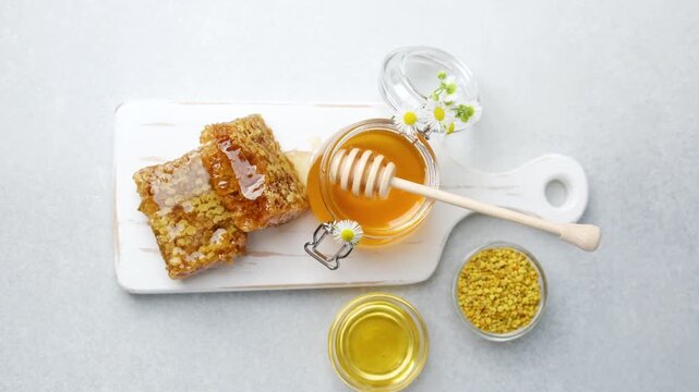 Honeycomb and honey in glass jars with bee pollen and daisies on a white board