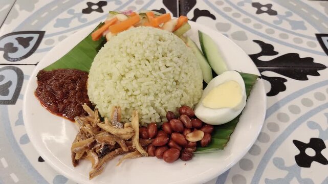 A plate of traditional Malaysian nasi lemak served with fragrant coconut rice, spicy sambal, crispy fried anchovies (ikan bilis), roasted peanuts, a boiled egg and fresh cucumber slices