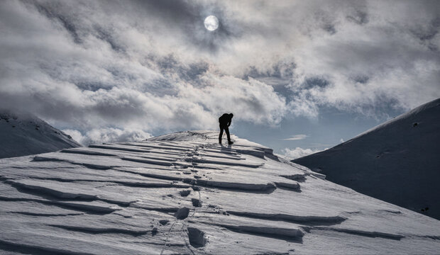 Lone Climber Standing on Snowy Ridge Beneath Dramatic Sky