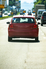Close view of a red hatchback moving in steady urban traffic Sunlight highlights the rear glass and taillights as the car follows the flow of vehicles down a straight avenue suggesting motion safety © Chornogirskyi
