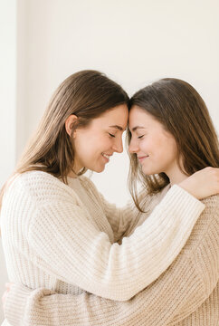 Two young women hugging and smiling in beige sweaters