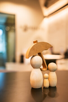 Family insurance and life protection concept with wooden umbrella covering wooden figure family on table with warm blurred background for safety and investment
