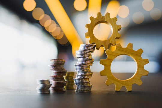 Financial mechanism and business integration concept with stack of coins and wooden gears on table with bokeh background representing economic growth and strategy