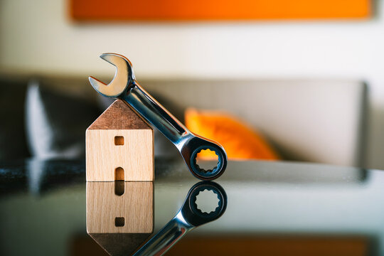 Home repair and maintenance real estate concept with metal wrench on wooden house model with reflection on black table for property inspection and renovation