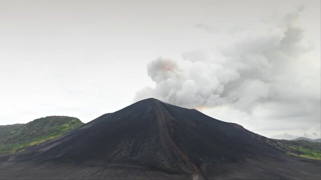 Mount Yasur volcano actively erupting in Vanuatu, releasing a plume of smoke and ash against a light sky, showing the raw dramatic power of nature on Tanna Island. Aerial view drone flight panorama