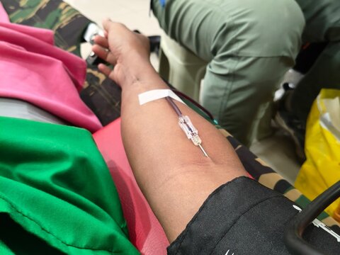 Close-up of a person donating blood with a needle inserted in the arm during a medical donation drive