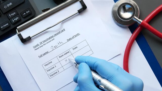 Doctor filling out covid 19 vaccination record card with blue gloves and stethoscope on desk