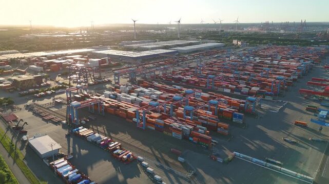 Hamburg, Germany - 01 July 2026: Aerial view of Container-Terminal-Altenwerder with rows of colorful shipping containers, gantry cranes, and wind turbines under a clear sky.