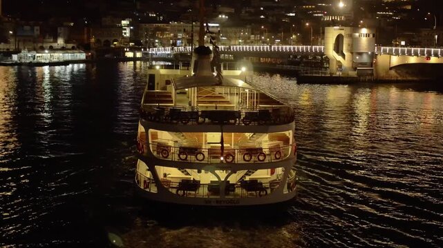 Istanbul, Istanbul, Turkiye - 30 June 2026: Aerial view of ferry boat cruising on the Bosphorus at night with illuminated city skyline and mosque silhouettes in the background.