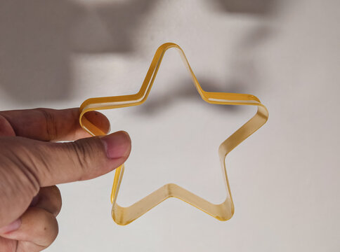 Hand Holding Yellow Star Cookie Cutter Against Neutral Shadowed Wall