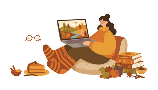Cozy autumn girl working on her laptop while sitting on a pillow surrounded by books, tea, and apple pie.
