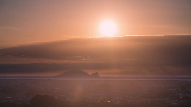 A beautiful golden sunrise over the Yilan city plain with the iconic Guishan Island on the horizon under a hazy morning sky in Taiwan.