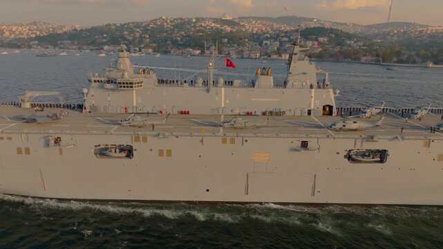 Istanbul, Istanbul, Turkiye - 30 June 2026: Aerial view of the TCG Anadolu naval ship sailing through the Bosphorus with helicopters on deck and the city skyline.
