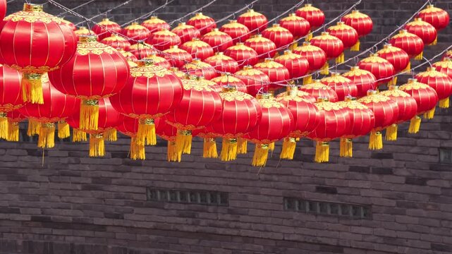Rows of vibrant red Chinese lanterns hanging against an ancient brick wall background.