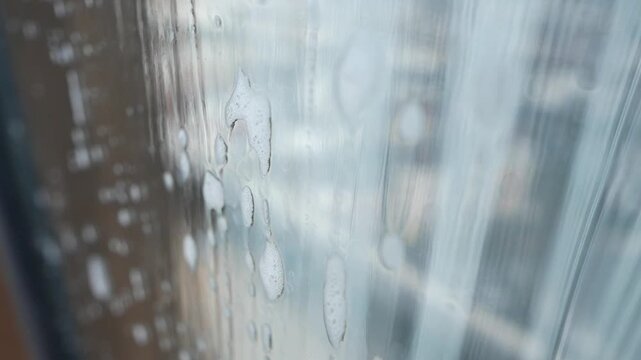 Close up of soapy window with water droplets slowly running down, blurred urban background