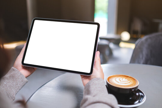 Mockup image of a woman holding digital tablet with blank white desktop screen in cafe