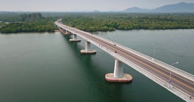 Aerial view Siri Lanta Bridge extending over river connecting Koh Lanta Yai and Koh Lanta Noi, surrounded by lush green mangrove forests and tropical landscape. Motorbikes driving road. Drone flight