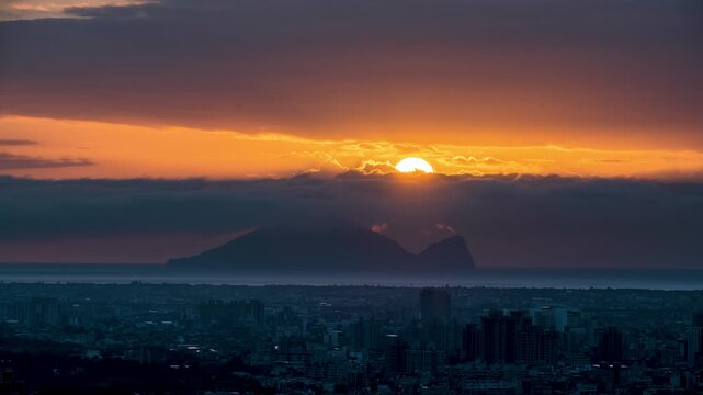 A scenic view of Yilan City at dawn with the sun rising behind Guishan Island, casting golden light through dramatic clouds in Taiwan.