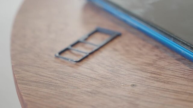 Close up of hand placing a sim card into a phone tray on wooden table