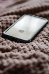 Smartfon w ochronnym etui leżący na miękkim, różowym kocyku. Przytulny klimat, praca zdalna i hybrydowa, komunikacja cyfrowa w domowym zaciszu. © Henryk Niestrój