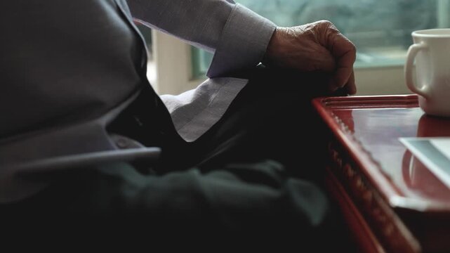 실내에서 찻상이 있는 자리에 앉아 있는 노인의 손과 상반신