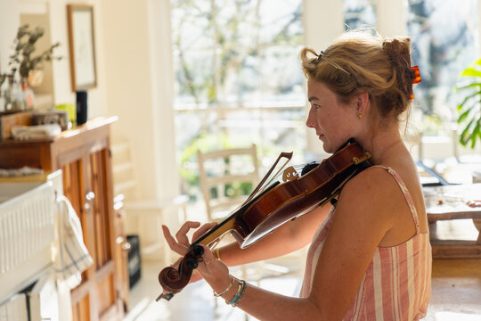 young woman playing violin in light filled kitchen