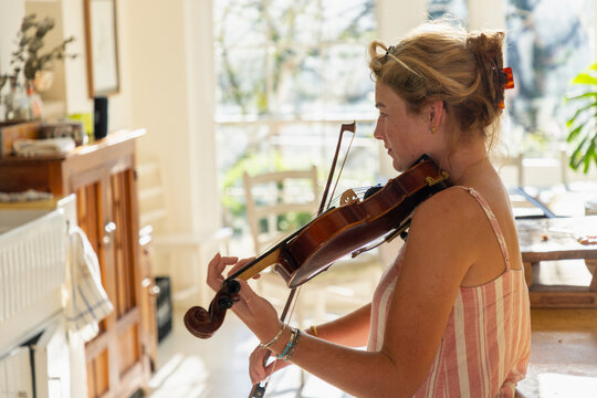 young woman playing violin in light filled kitchen
