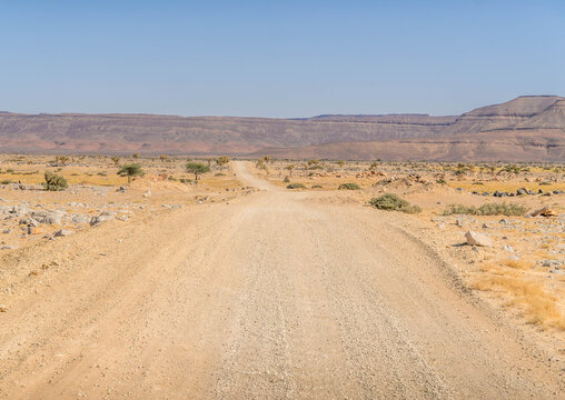 Desert road in Adrar Plateau, West Africa, in Mauritania landscape with sandstone rocks in the horizon, nearby Atar.
