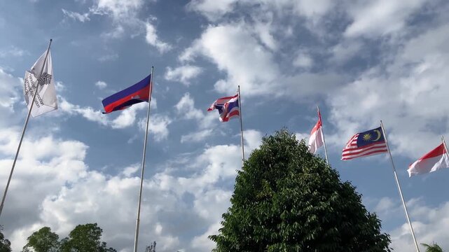 Slow motion clip of multiple Southeast Asian and Asia Pacific country flags waving proudly on flagpoles against a beautiful sunny blue sky with white clouds. International diplomacy concept.