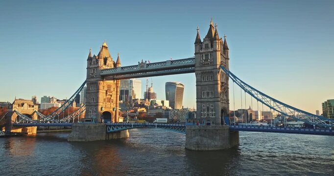 Iconic Tower Bridge standing majestically over the River Thames with the cityscape and modern skyscrapers of London illuminated by the warm golden light of the setting sun. Aerial view drone panorama