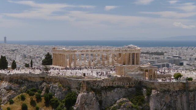 Aerial view of the Parthenon atop the Acropolis in Athens, Greece, with crowds of visitors exploring the ancient ruins above the sprawling city.