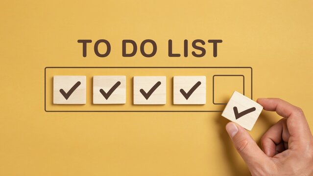 To do list with hand placing final check mark on wooden block over yellow background.
