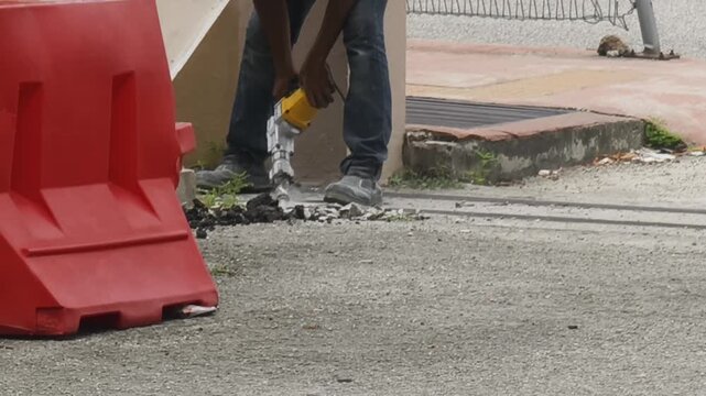 Worker breaking old asphalt concrete pavement with a power demolition hammer tool during road maintenance.