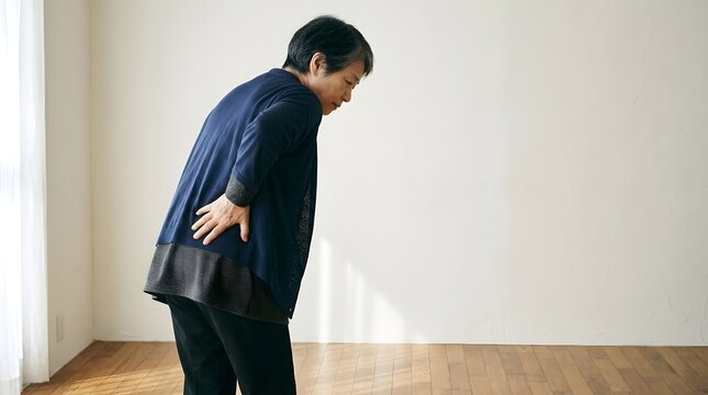 腰の痛みに耐えながら前かがみになるシニア女性