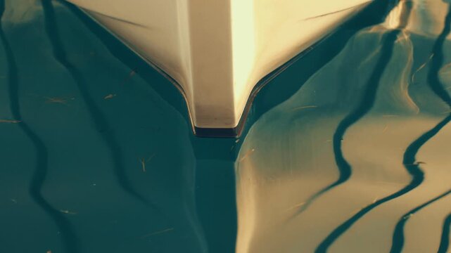 Cinematic vintage abstract footage capturing a close-up view of a white boat bow cutting through calm water, creating soft and artistic surface reflections.
