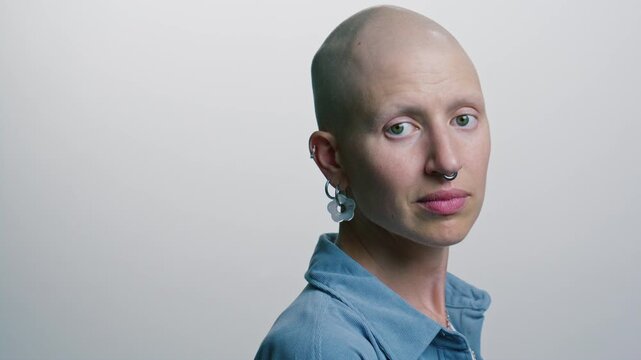 Young female oncology patient with bald head looking at camera against clean white studio background. Video portrait