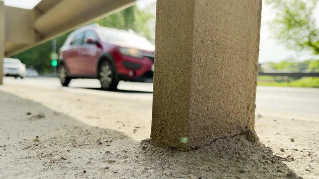 Cars drive fast down a sunny metropolitan street next to a concrete support pillar. Their rapid movement creates the loud, continuous roar of city traffic.
