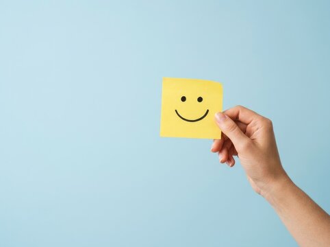 Hand holding a yellow sticky note with a happy face for world mental health day awareness