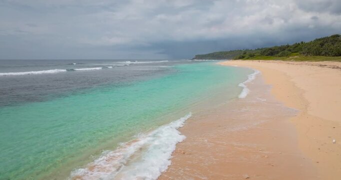 White sand beach on Port Resolution with clear turquoise water and gentle ocean waves rolling to the shore under a dramatic cloudy sky, creating serene tropical landscape of Tana Island. Exotic travel