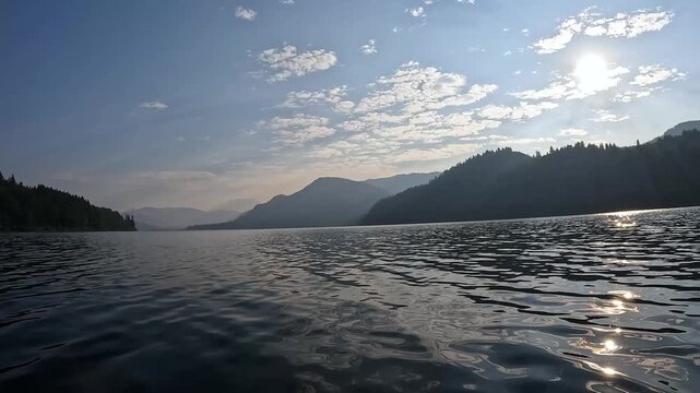 4K smooth stabilized action camera footage while kayaking on Yale Lake, Washington, USA with gentle waves, surrounding forested mountains and morning sunlight reflecting on the water during summer