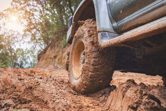 Offroad 4x4 vehicle with mud-covered tire on a red dirt road through the forest, capturing adventure driving, muddy trail, overland travel, rough terrain, and nature.