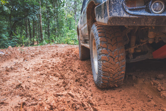 Close-up of a muddy offroad tire on a 4x4 vehicle driving along a red clay forest trail, showcasing rugged adventure, overland travel, rough terrain, and outdoor exploration.