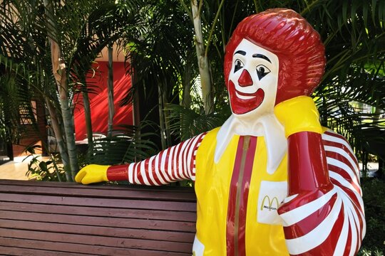 Bangkok, Thailand - January 12, 2026: Ronald McDonald statue sitting on a wooden bench outdoors near green plants.